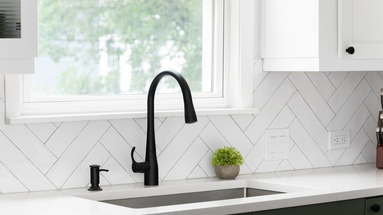 A white herringbone pattern backplash installed in a white kitchen with a black sink