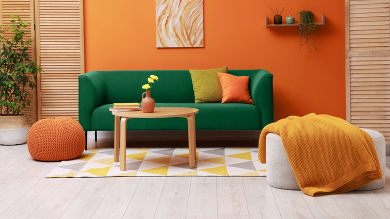 Stylish living room with comfortable green sofa and bright orange wall