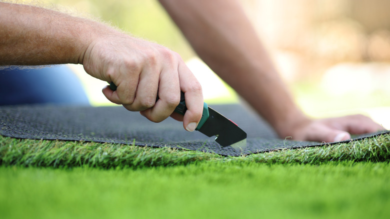 Hands cutting artificial turf during installation