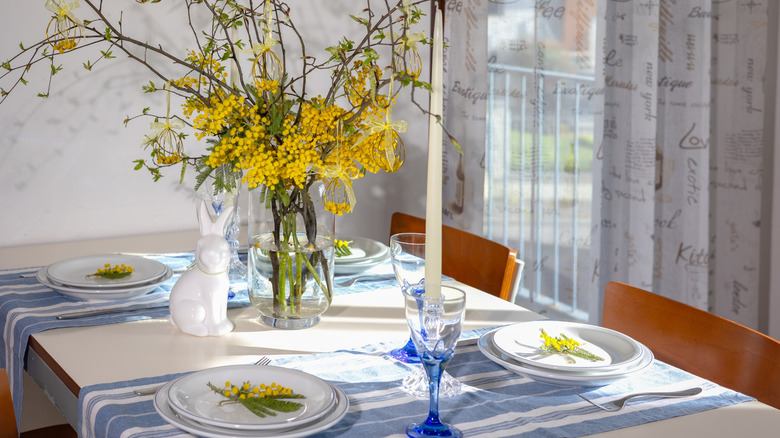 A spring dinner table is set up with yellow flowers and two blue and white runners arranged like placemats.
