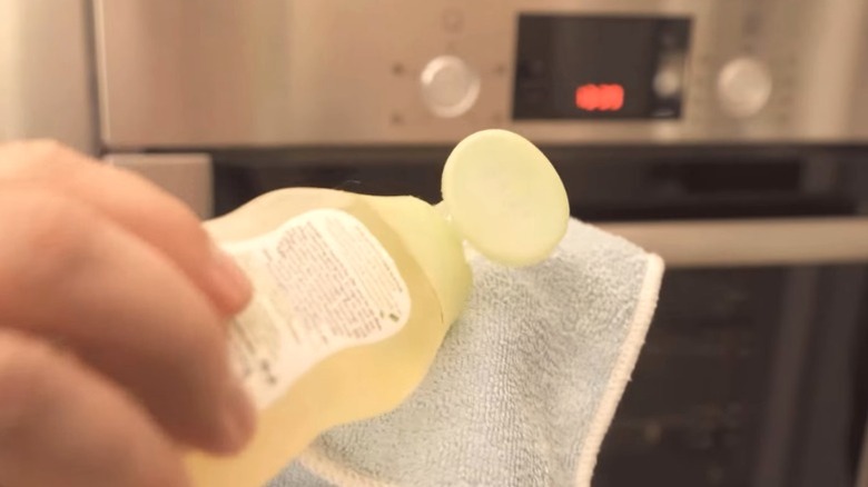 Person applying baby oil to microfiber cloth to wipe down stainless steel oven
