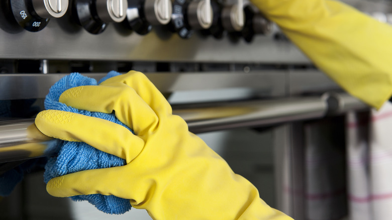 Close up of person with yellow gloves cleaning oven