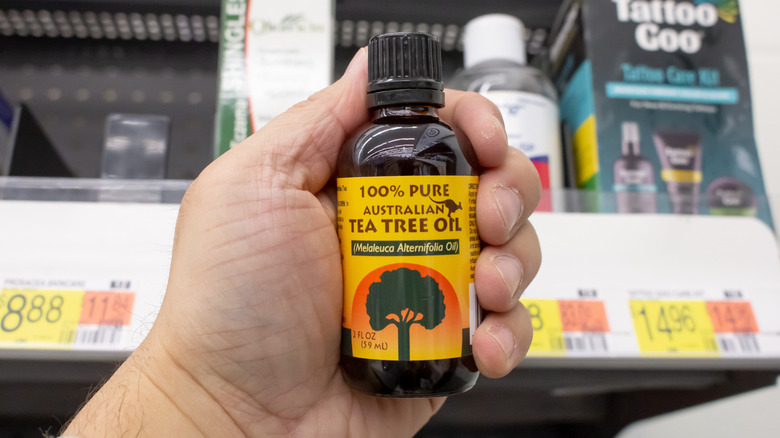A person holds a bottle of tea tree oil in front of grocery store shelves.