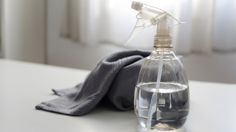 spray bottle filled with vinegar in front of cleaning cloth sitting on a table