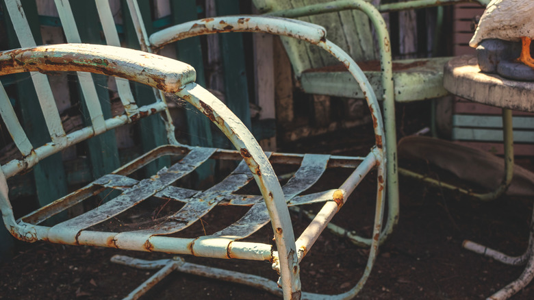Iron patio furniture is sitting in the dirt outside, covered in rust and spider webs.