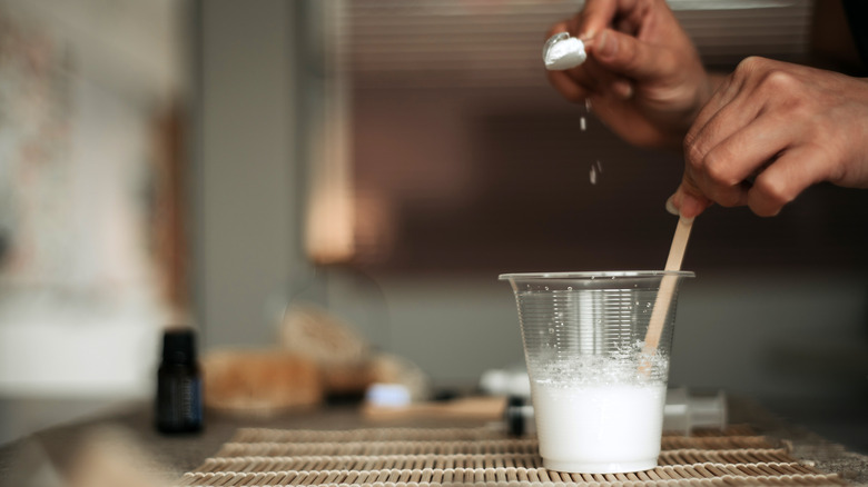 Hand pouring baking soda into a cup of water to make a paste