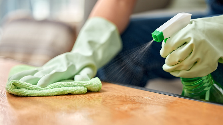 Close-up of a person cleaning a wooden table with a cloth and spray cleaner