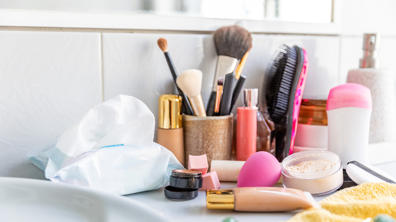 cluttered bathroom counter near sink with makeup, brushes, and other bathroom essentials