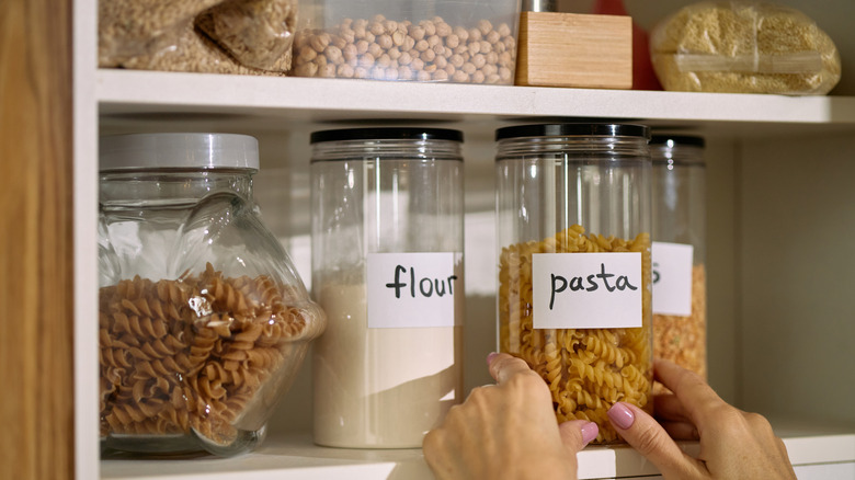 Person putting dry ingredients on pantry shelving in glass jars