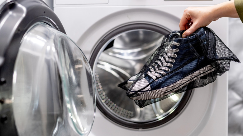 A hand placing shoes into a dryer inside of a mesh bag.