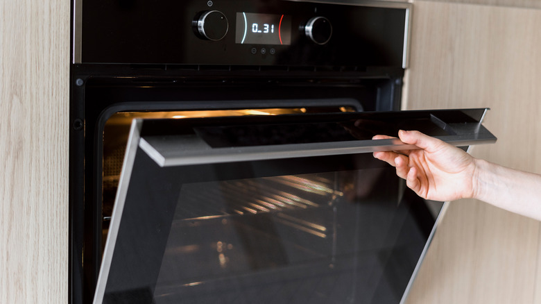 Close up of a black wall oven being opened by someone's hand