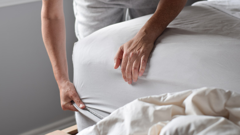person making bed by tucking sheet around corner