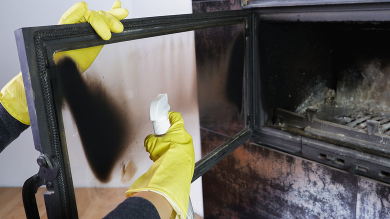 Person with yellow rubber globes cleaning fireplace glass with a spray