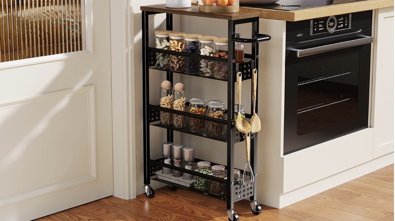 A narrow black rolling storage cart full of spices and jarred goods next to kitchen counters