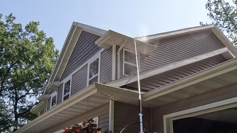 Extension pole being used to spray water into gutters of a house