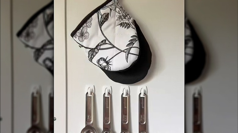 Measuring spoons and pot holder hung on Dollar Tree self-adhesive hooks inside a cabinet door