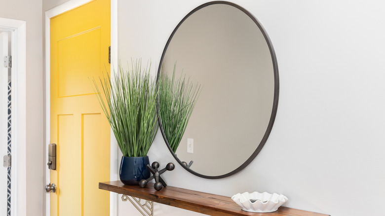 A round mirror above a modern wood shelf.