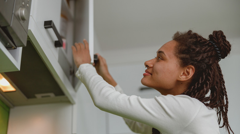Joyful female with braids opening cupboard indoor