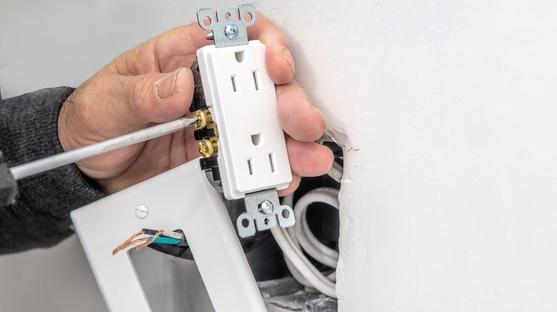 An electrician connects electrical wires to an outlet before installing it