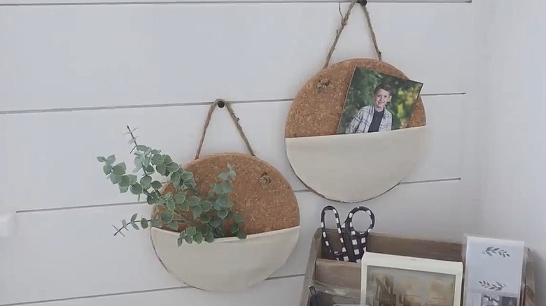 Two wall organization pouches made from IKEA cork trivets hanging on a wood wall next to an office organizer