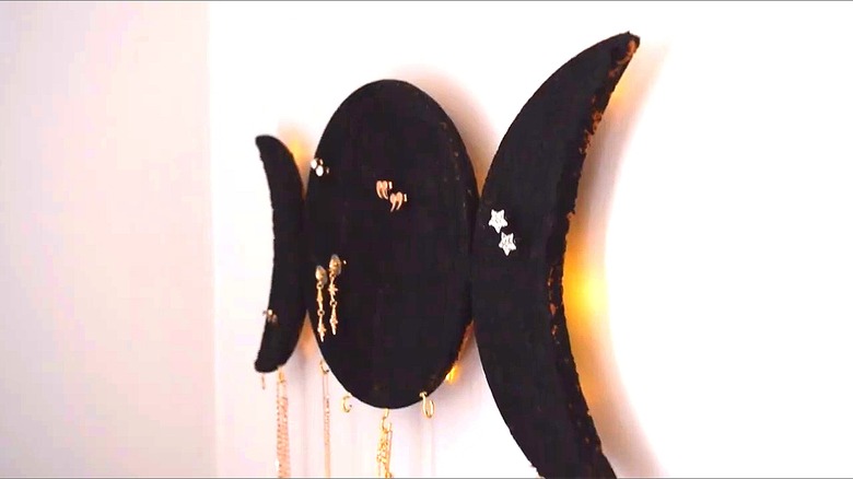 IKEA trivets painted black with two end pieces cut like crescents and jewelry hanging on the holder