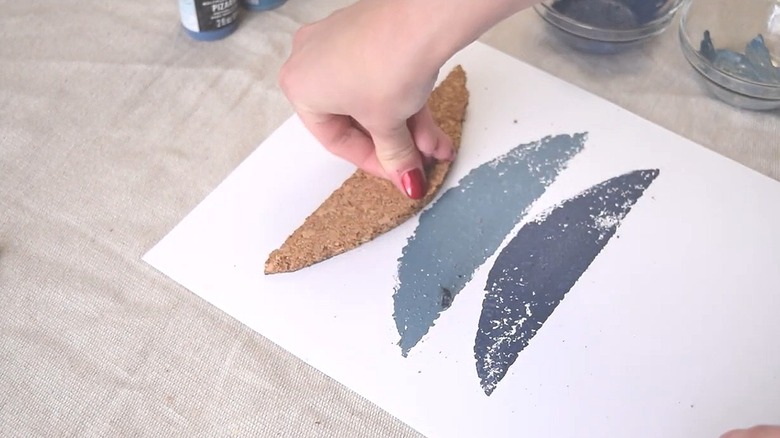 Person pressing a piece of cork trivet onto a paper as a stamp to create a painted design