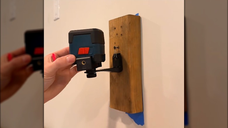 Hand holds DIY laser level mount against wall