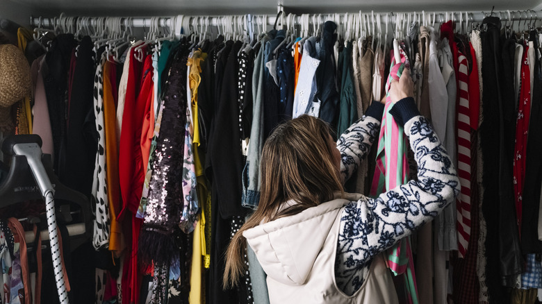 Woman placing a large amount of clothes in a closet in her room