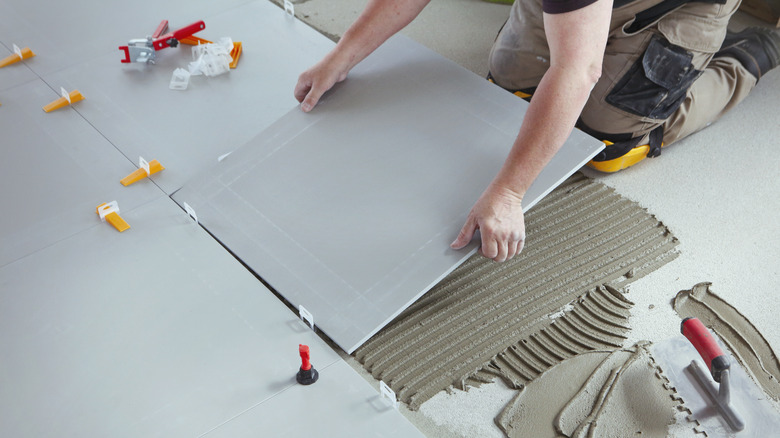 person laying large gray tiles on grout