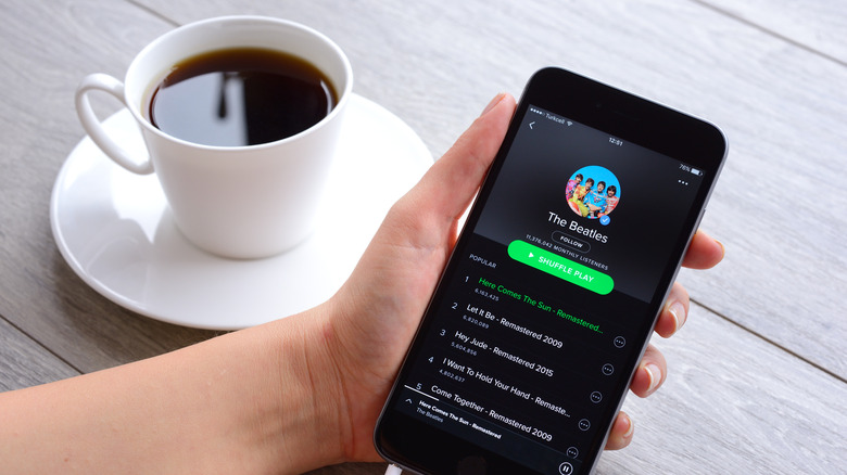 A hand holds a phone showing Spotify next to a cup of black coffee