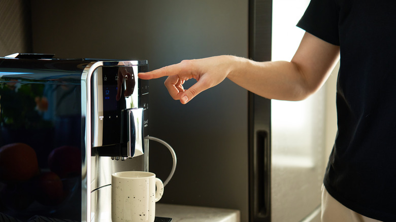 A person pushes a button on a coffee machine at home