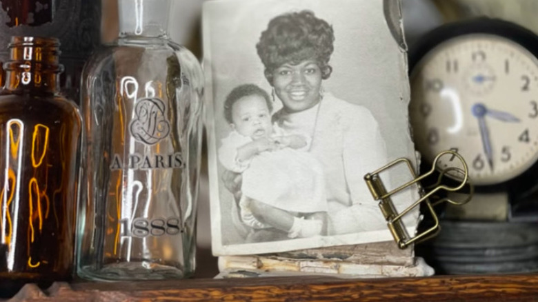 Photo clamped onto a painted hinge on a shelf with a clock and glass bottles
