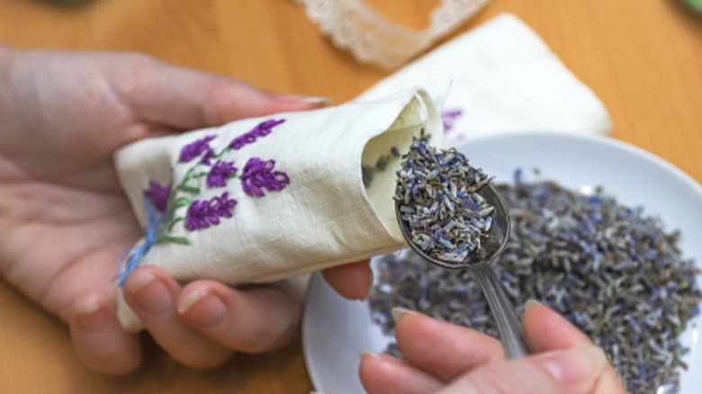 Hands scooping lavender into a fabric satchet.
