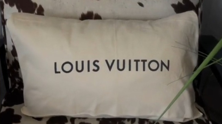 A throw pillow made from an old Louis Vuitton dust bag sitting on a cowhide chair.