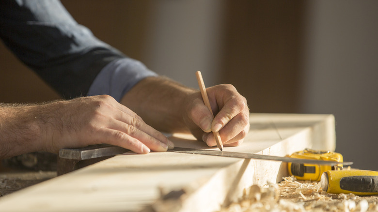 person marking measurement on wood