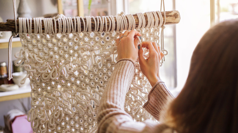 A person is shown from behind while working on a macrame hanging