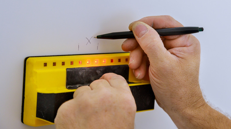 Using a stud finder to help ensure closet shelves are properly attached to the wall