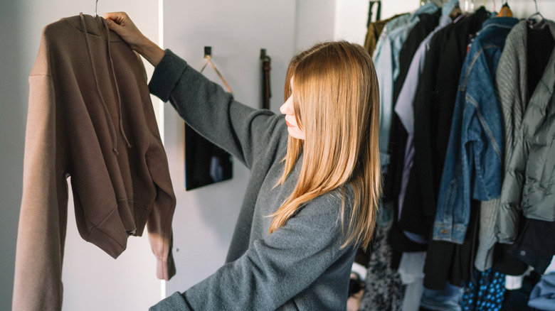 young woman examining fall colored hoodie in closet