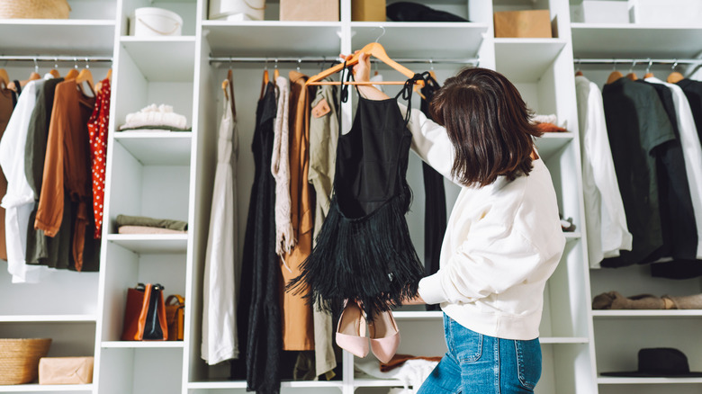 woman examining black dress and pink shoes in closet