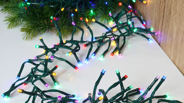 A multi-colored strand of cluster twinkle lights lays on the floor near the base of a Christmas tree