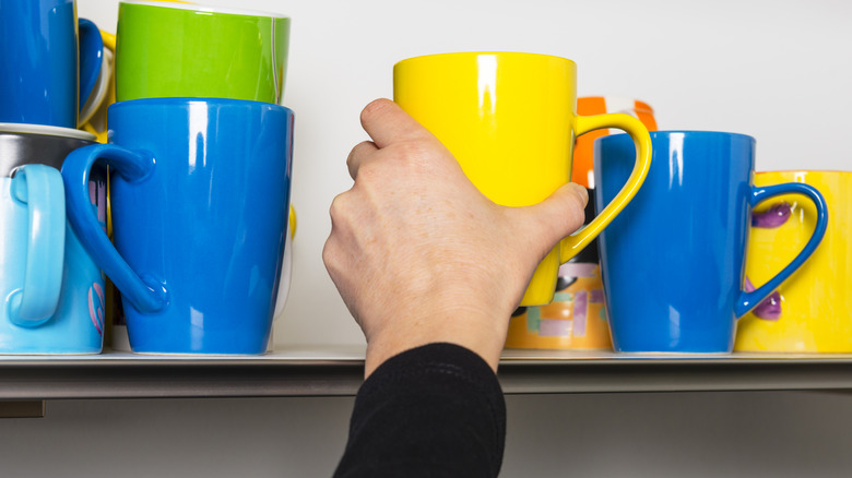 person puts a mug onto a shelf with more mugs