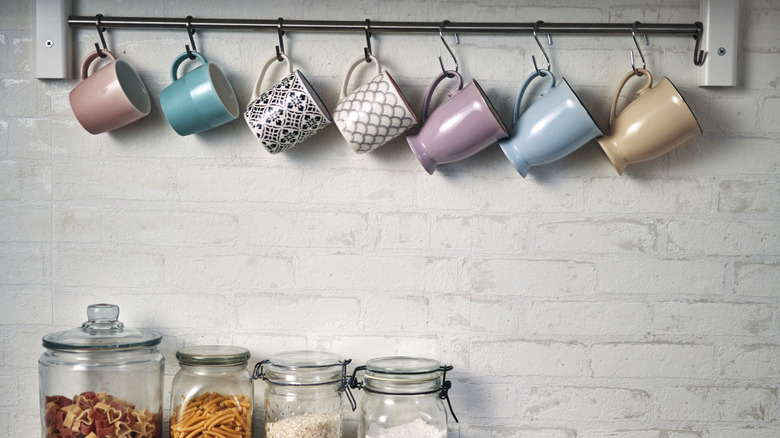 Mugs hanging from hooks on a white painted brick wall with kilner jars below.