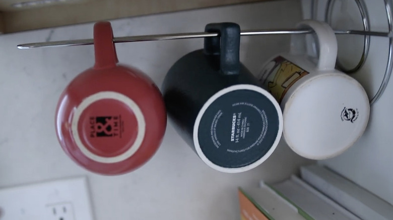 Coffee mugs hanging off a vertically installed kitchen roll holder.