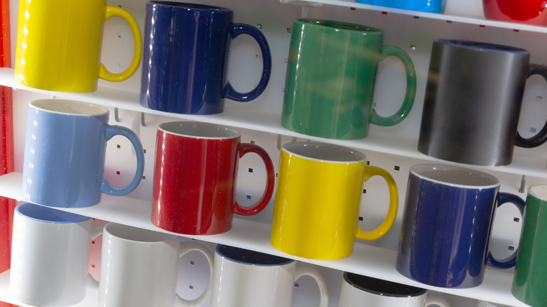 Different coloured coffee mugs lined up on shelves.