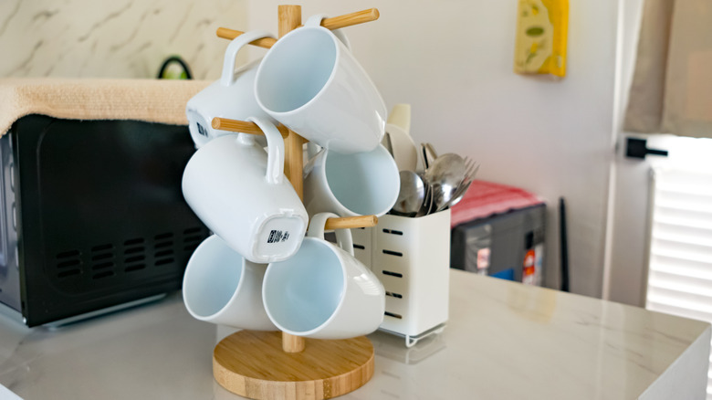 A mug holder tree on a kitchen cabinet with a cutlery organiser behind it.