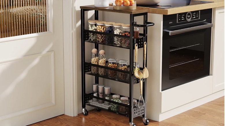 A narrow black rolling storage cart full of spices and jarred goods next to kitchen counters