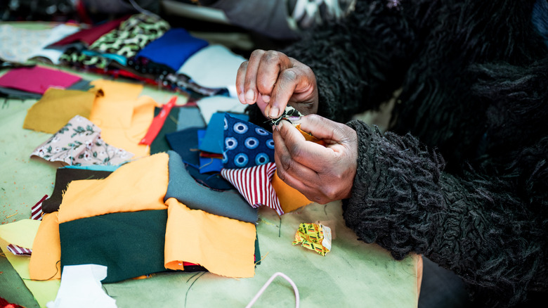 A pair of dark-skinned hands sew fabric pieces together.