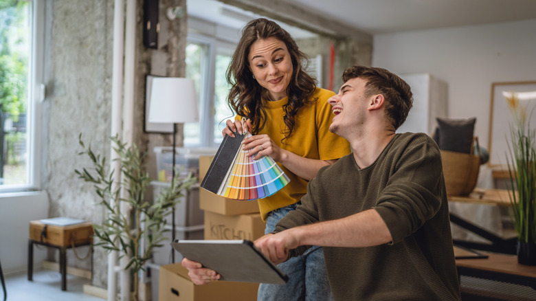 A woman holding paint samples discusses furniture colors with a man holding a tablet.