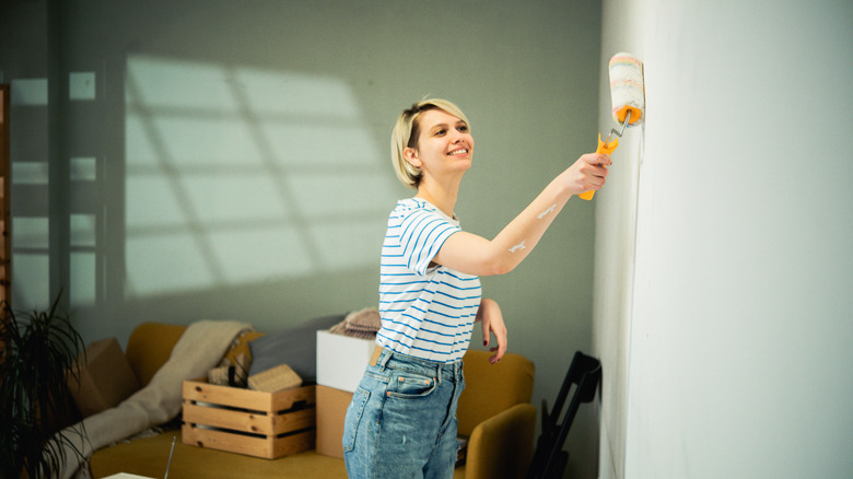 A smiling young woman paints an interior wall sage green