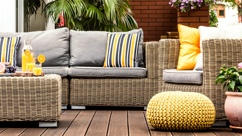 Colorful cushion covers on patio furniture and a yellow pouf near it
